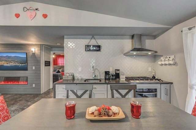 kitchen with wall chimney exhaust hood, wall oven, dark countertops, vaulted ceiling, and stainless steel gas cooktop