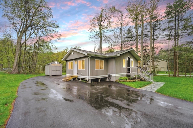 view of front of house featuring a storage shed, an outbuilding, driveway, a front yard, and roof with shingles