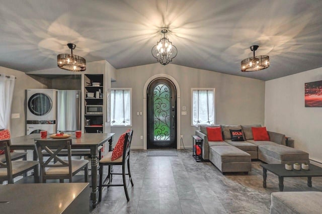 living area with stacked washer / drying machine, a chandelier, baseboards, and vaulted ceiling