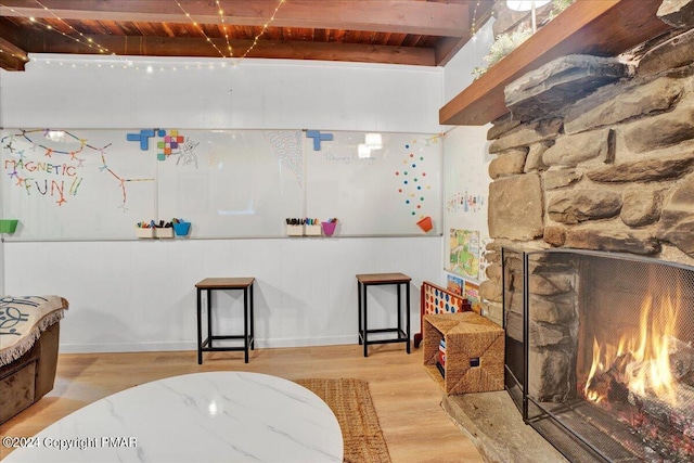 interior space featuring a stone fireplace, beamed ceiling, wooden ceiling, and wood finished floors