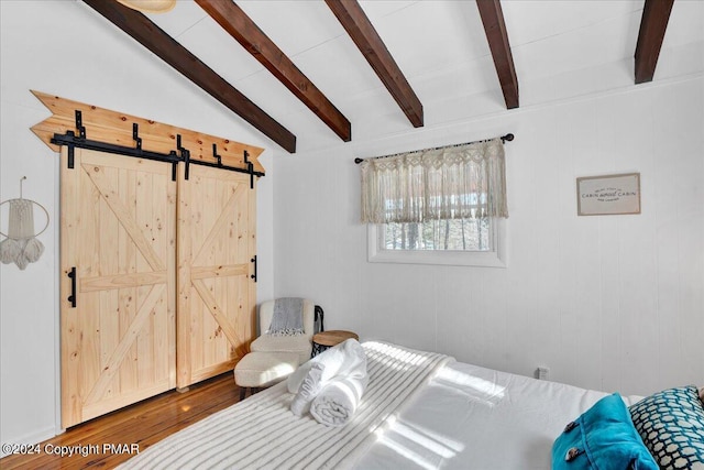 bedroom with lofted ceiling with beams, a barn door, and wood finished floors