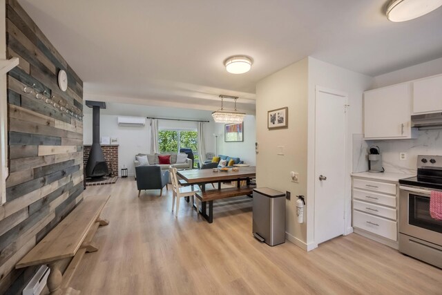 130 Cross Country Ln, Tannersville, PA 18372 - kitchen featuring stainless steel range with electric stovetop, a wall unit AC, under cabinet range hood, a wood stove, and white cabinets
