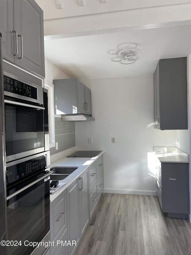 kitchen with gray cabinetry, black electric stovetop, light wood-type flooring, decorative backsplash, and stainless steel double oven