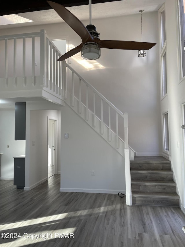 stairway with baseboards, wood finished floors, a towering ceiling, and a ceiling fan