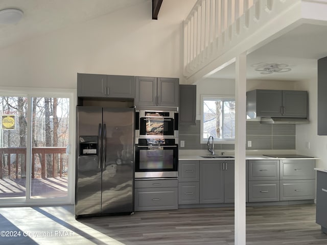 kitchen with high vaulted ceiling, stainless steel double oven, gray cabinets, a sink, and fridge with ice dispenser