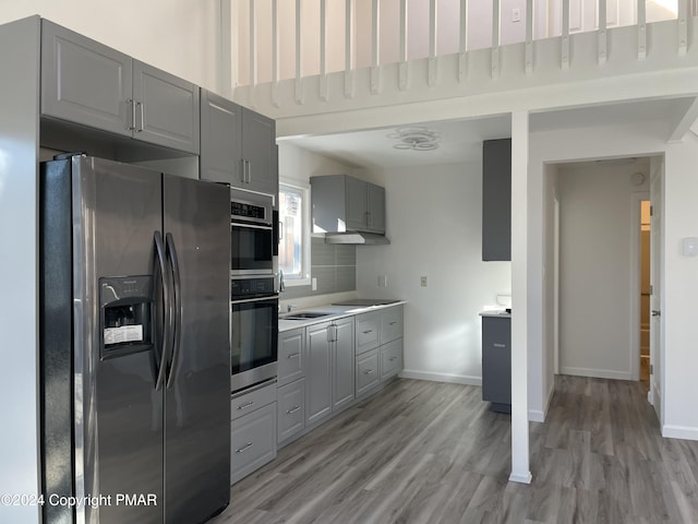 kitchen with baseboards, light wood finished floors, gray cabinetry, stainless steel appliances, and light countertops