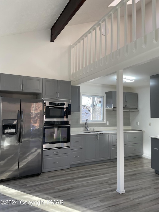 kitchen featuring beamed ceiling, gray cabinetry, stainless steel appliances, and a sink