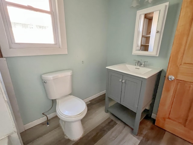 half bathroom with toilet, baseboards, wood finished floors, and vanity