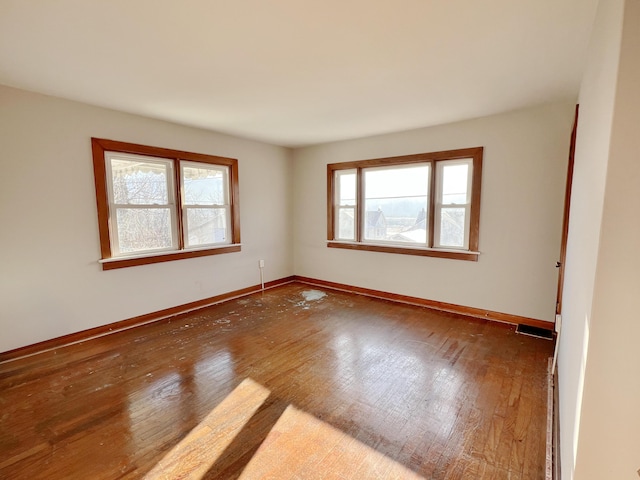 unfurnished room with hardwood / wood-style floors, visible vents, and baseboards