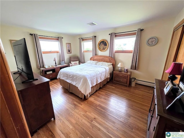 bedroom with a baseboard heating unit and wood finished floors