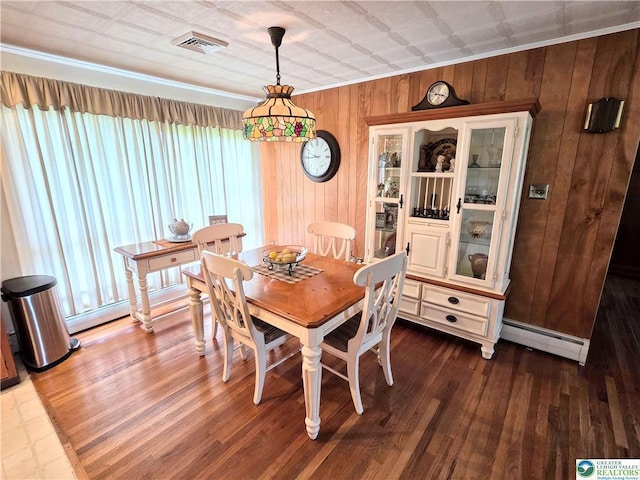 dining space with baseboard heating, plenty of natural light, wooden walls, dark wood-style floors, and crown molding