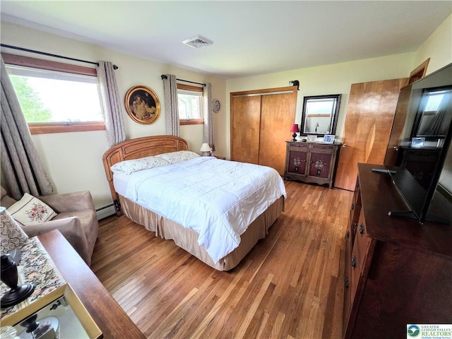bedroom with light wood finished floors, a baseboard radiator, and a closet