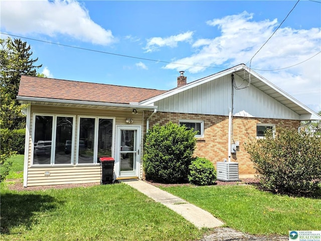 view of front facade with central AC unit, a chimney, a front yard, and brick siding