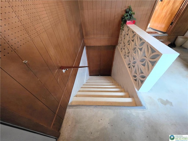 stairway with unfinished concrete floors and wooden walls