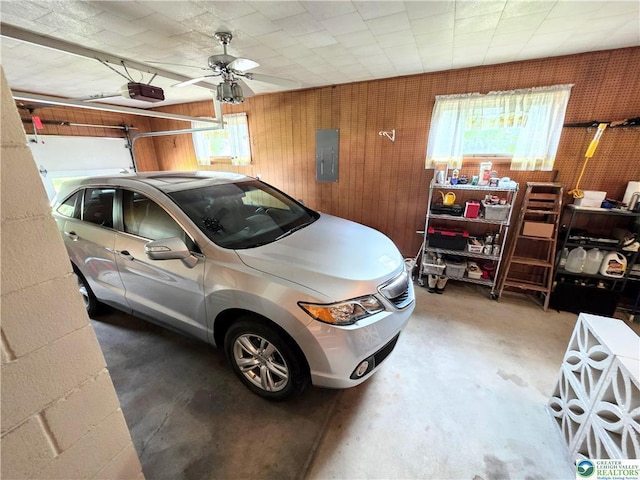 garage featuring electric panel, a garage door opener, a ceiling fan, and wood walls