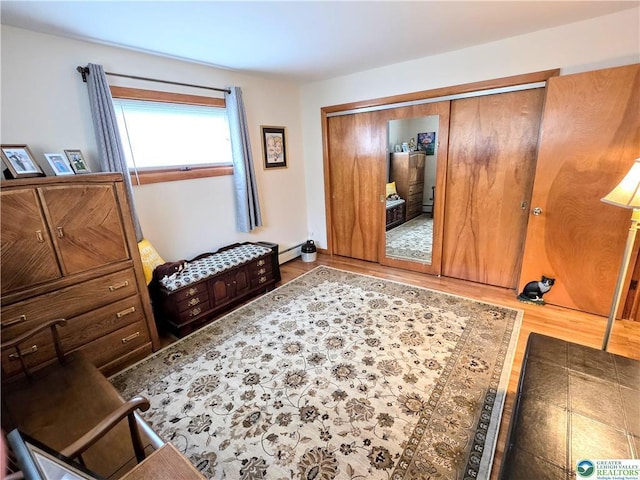 bedroom with wood finished floors, baseboard heating, and a closet