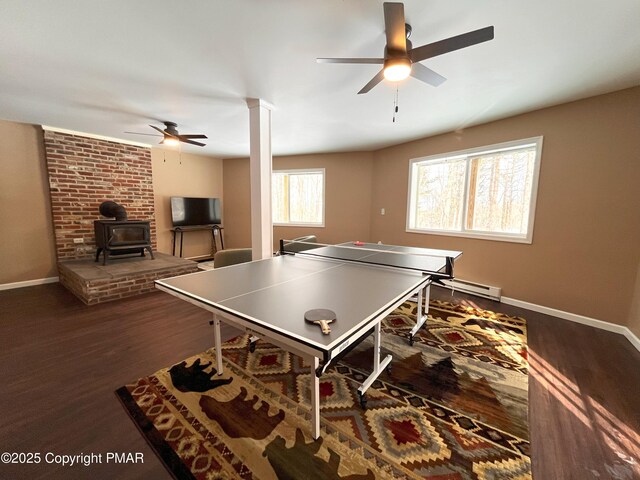 rec room featuring dark wood-type flooring, ornate columns, ceiling fan, and a wood stove