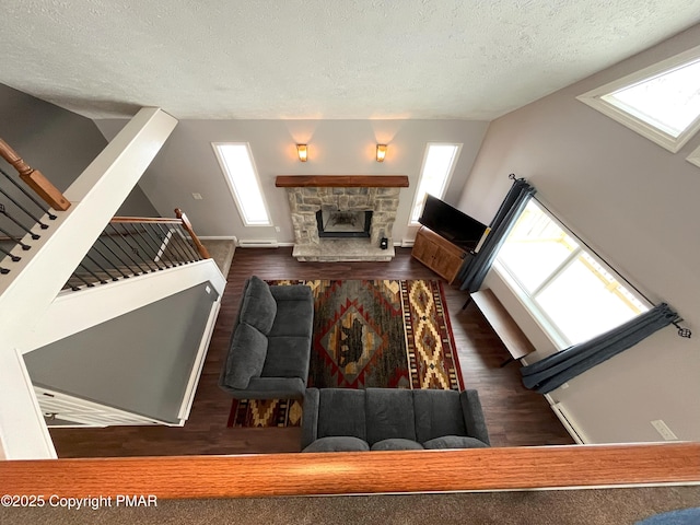 living room featuring dark hardwood / wood-style floors, a stone fireplace, and a textured ceiling