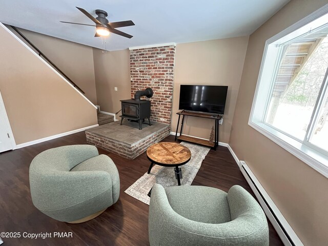 living room with a wood stove, dark hardwood / wood-style floors, ceiling fan, and baseboard heating