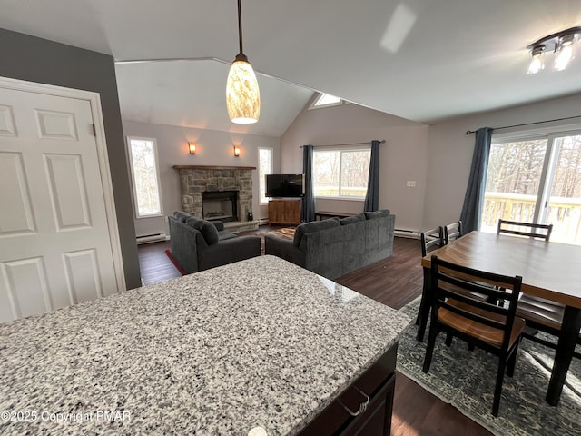 kitchen featuring lofted ceiling, decorative light fixtures, dark hardwood / wood-style floors, a fireplace, and light stone countertops