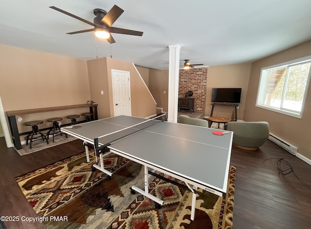 game room featuring dark hardwood / wood-style flooring, a wood stove, ceiling fan, and baseboard heating