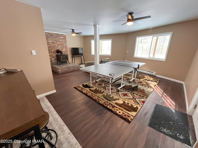 recreation room with ceiling fan, dark hardwood / wood-style floors, ornate columns, and a wood stove