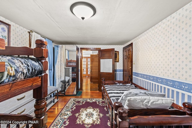 bedroom featuring wood finished floors, wainscoting, and wallpapered walls