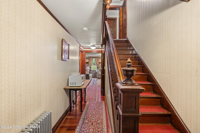 stairs with radiator, wallpapered walls, baseboards, ornamental molding, and wood finished floors