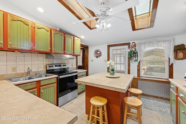 kitchen with a ceiling fan, a sink, stainless steel range with electric cooktop, light countertops, and under cabinet range hood