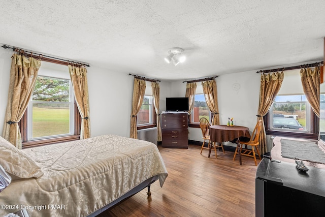 bedroom featuring multiple windows, a textured ceiling, radiator heating unit, and wood finished floors