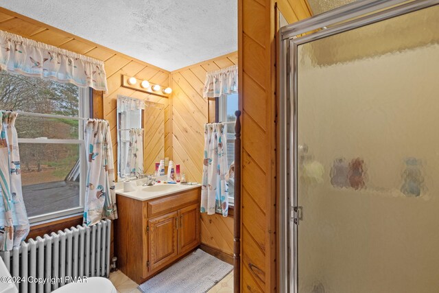 full bathroom featuring wood walls, radiator heating unit, vanity, a stall shower, and a textured ceiling