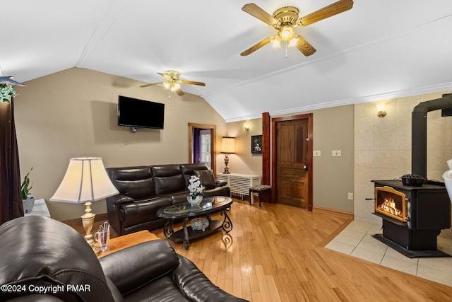 living area with lofted ceiling, a wood stove, a ceiling fan, and light wood-type flooring