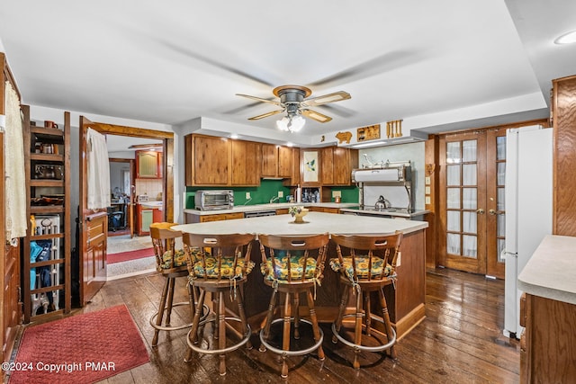 kitchen with brown cabinetry, dark wood-type flooring, light countertops, and freestanding refrigerator