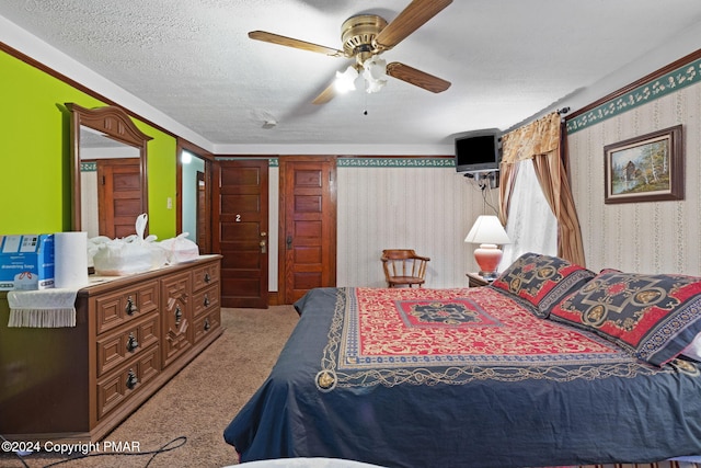 carpeted bedroom featuring a textured ceiling, wallpapered walls, and a ceiling fan