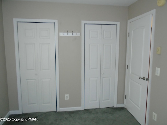 unfurnished bedroom featuring dark colored carpet, baseboards, and two closets