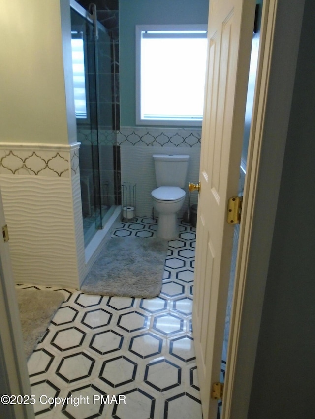 bathroom featuring a stall shower, toilet, a wainscoted wall, tile patterned floors, and tile walls