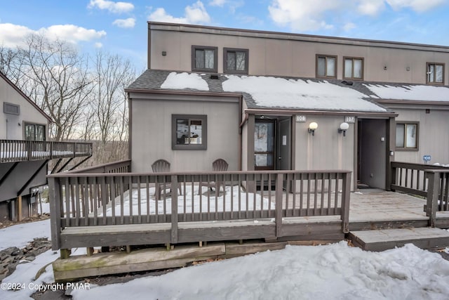 snow covered back of property featuring a shingled roof and a wooden deck