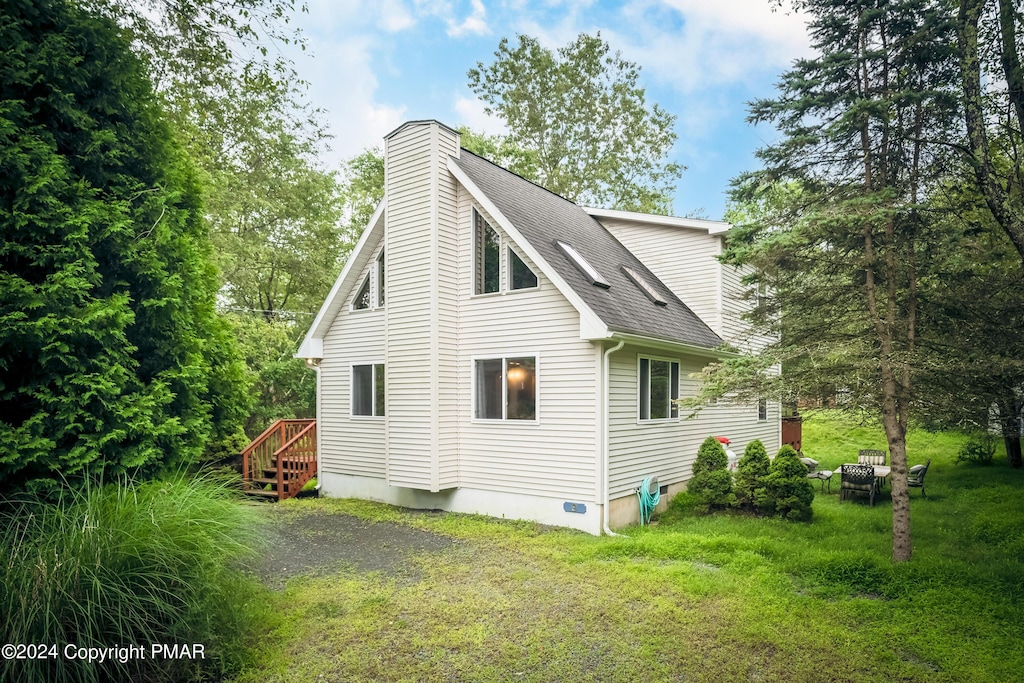 back of property with a shingled roof, driveway, a lawn, and a chimney