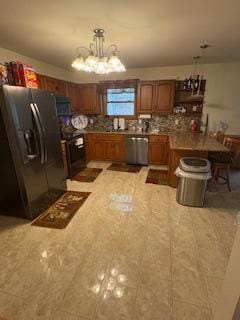 60 Arbutus Ln, East Stroudsburg, PA 18302 - kitchen featuring stainless steel appliances, a chandelier, brown cabinetry, light stone countertops, and pendant lighting