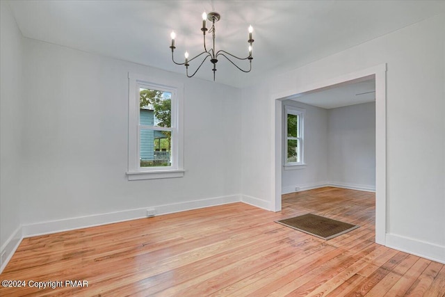 spare room featuring light wood finished floors, a chandelier, and baseboards