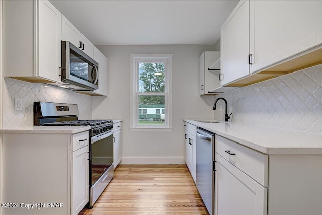 kitchen with a sink, light wood-style floors, backsplash, baseboards, and appliances with stainless steel finishes