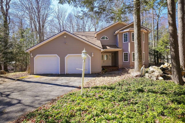traditional-style house with driveway, an attached garage, and a shingled roof