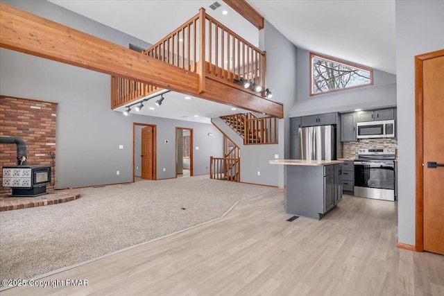 kitchen featuring a wood stove, appliances with stainless steel finishes, gray cabinets, a high ceiling, and backsplash