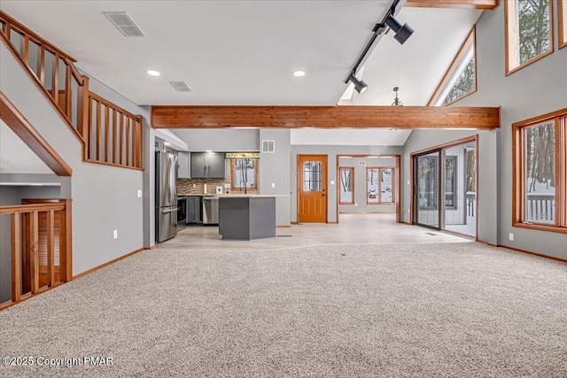 unfurnished living room featuring light carpet, beam ceiling, rail lighting, and a high ceiling