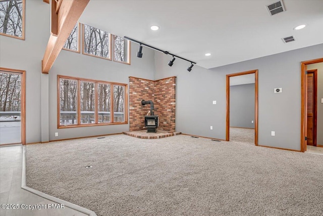 unfurnished living room with light colored carpet, a towering ceiling, track lighting, and a wood stove