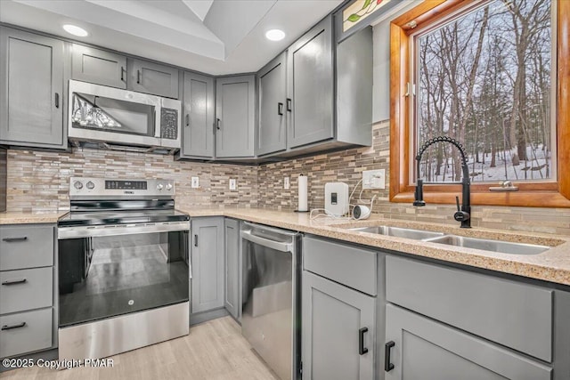 kitchen with gray cabinets, appliances with stainless steel finishes, sink, decorative backsplash, and light stone counters