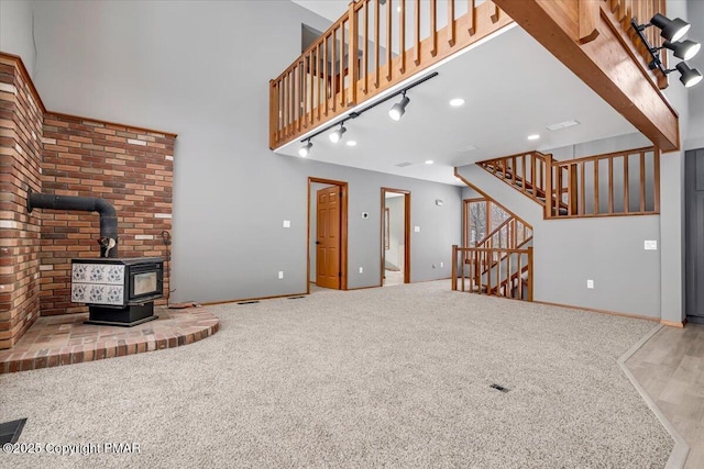 unfurnished living room with a towering ceiling, carpet flooring, rail lighting, and a wood stove