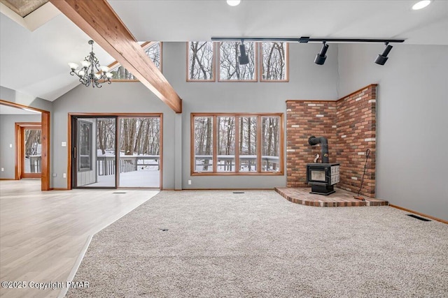 unfurnished living room featuring plenty of natural light, high vaulted ceiling, and a wood stove