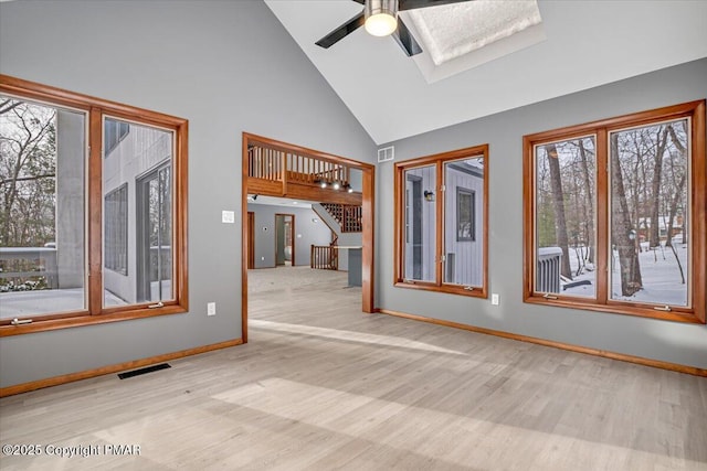 spare room with ceiling fan, light wood-type flooring, high vaulted ceiling, and a skylight