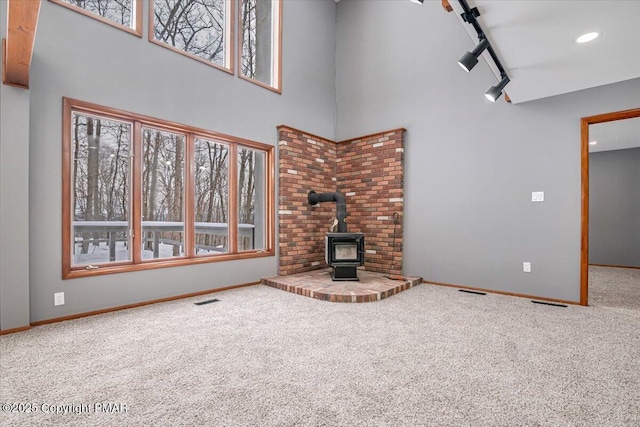 unfurnished living room featuring a towering ceiling, rail lighting, carpet floors, and a wood stove